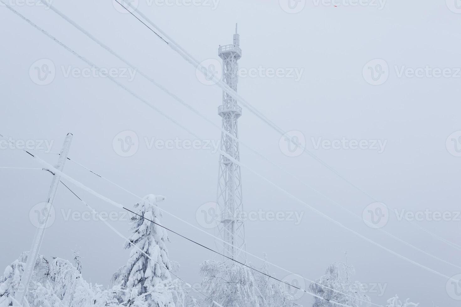 frosted cell tower and electric wires over a snowy forest on top of a mountain against a winter sky photo