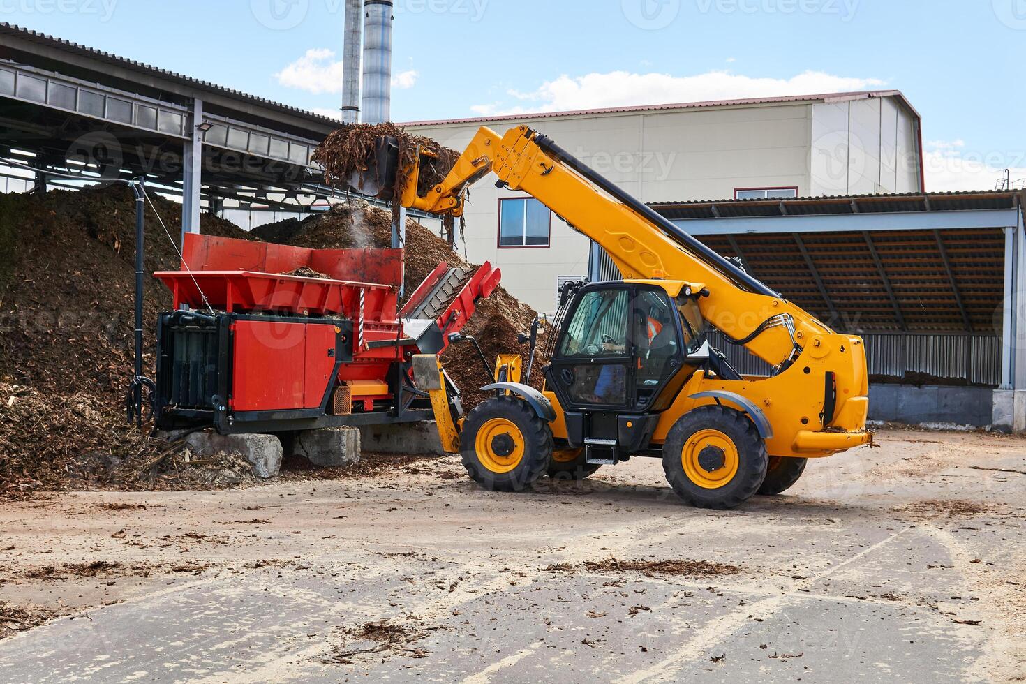 bucket loader loads tree bark into an industrial tree chipper photo