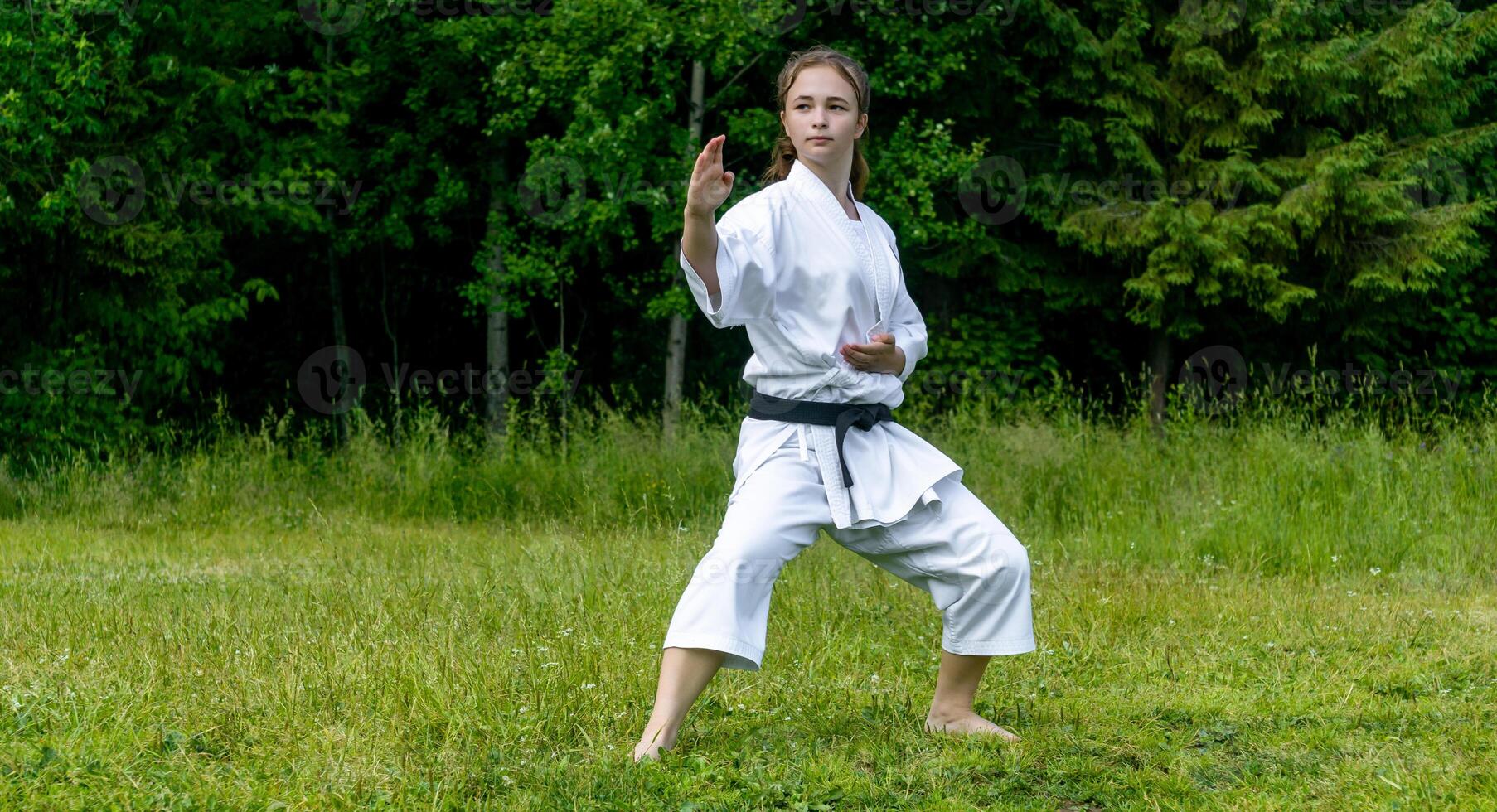 teenage girl training karate kata outdoors, performs soto uke or outside block in kakutsu dachi stand photo