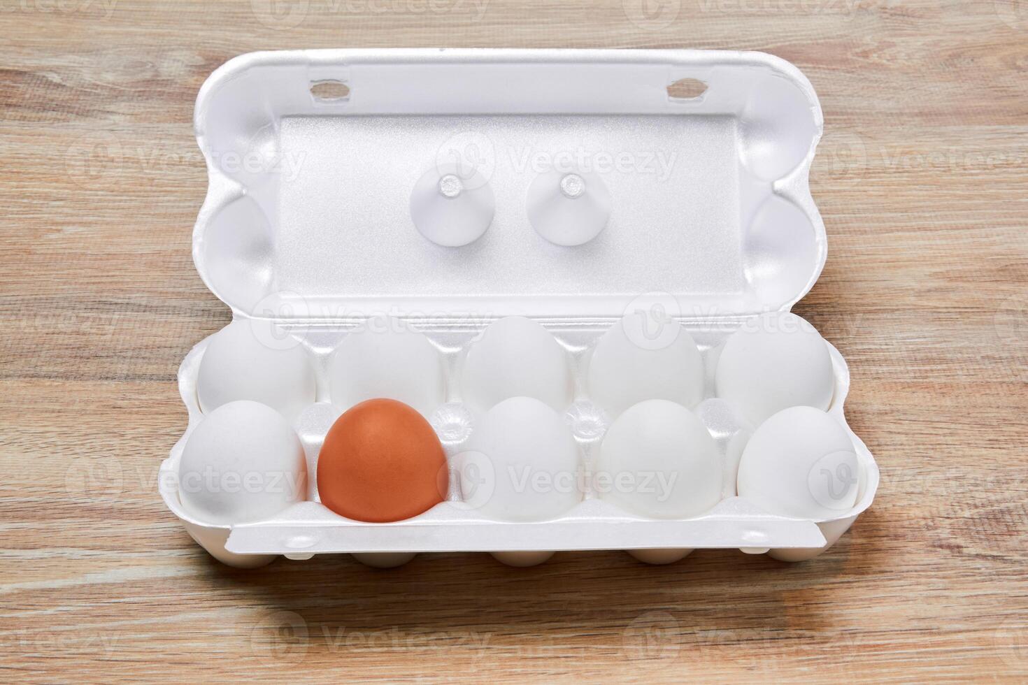 egg crate with nine white eggs and one brown on a wooden table surface photo