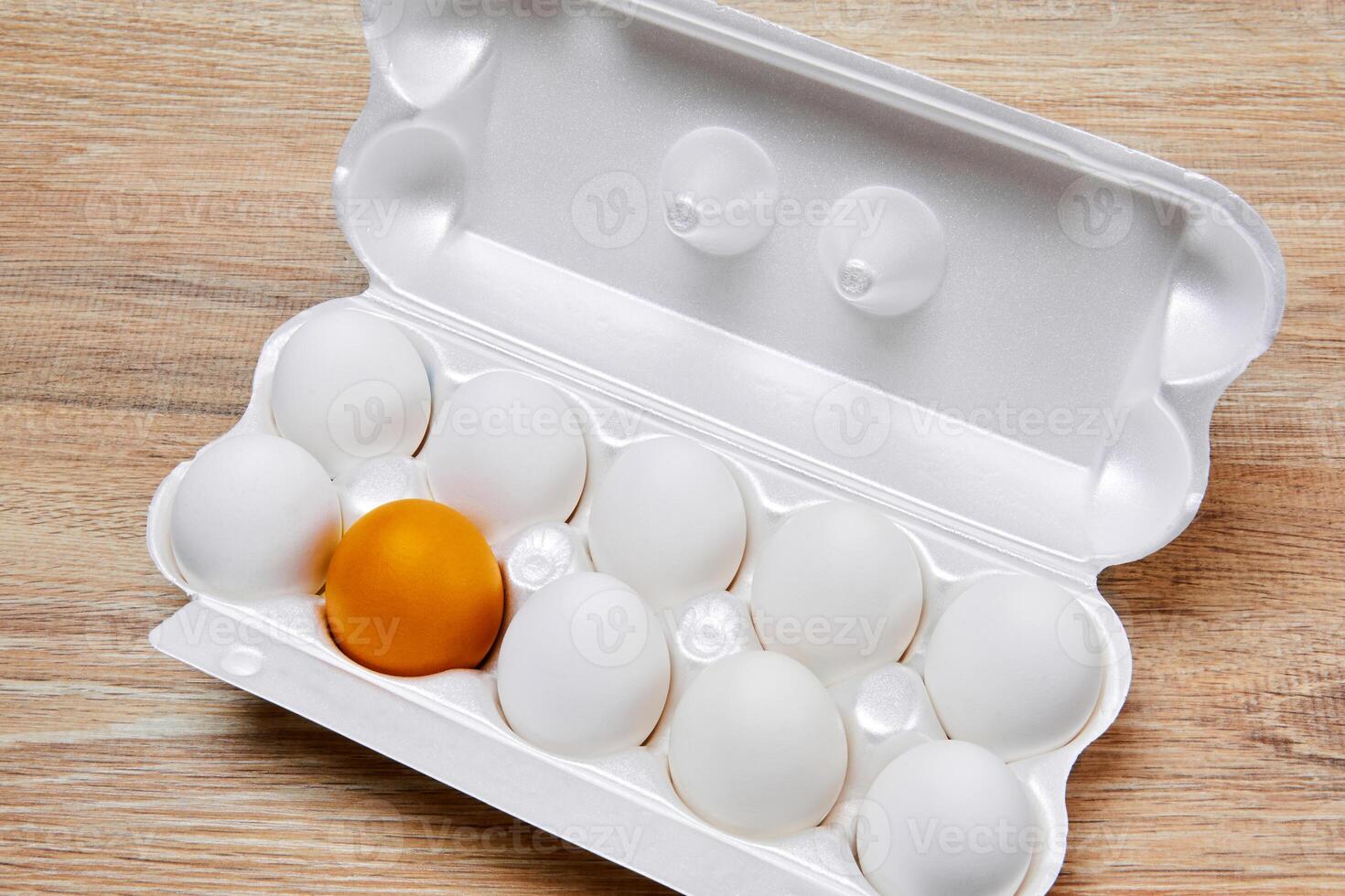 egg crate with nine white eggs and one golden yellow on a wooden table surface photo