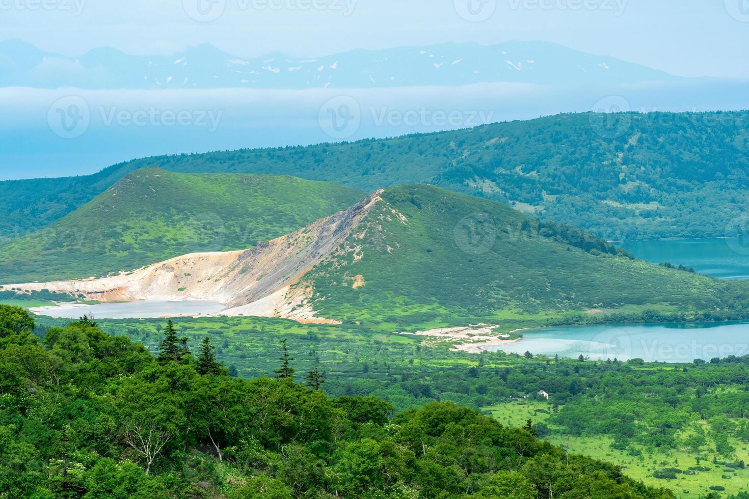 landscape of Kunashir island, geothermal lakes among lava domes in the center of the caldera of Golovnin volcano, Hokkaido island is visible in the distance in the sea photo