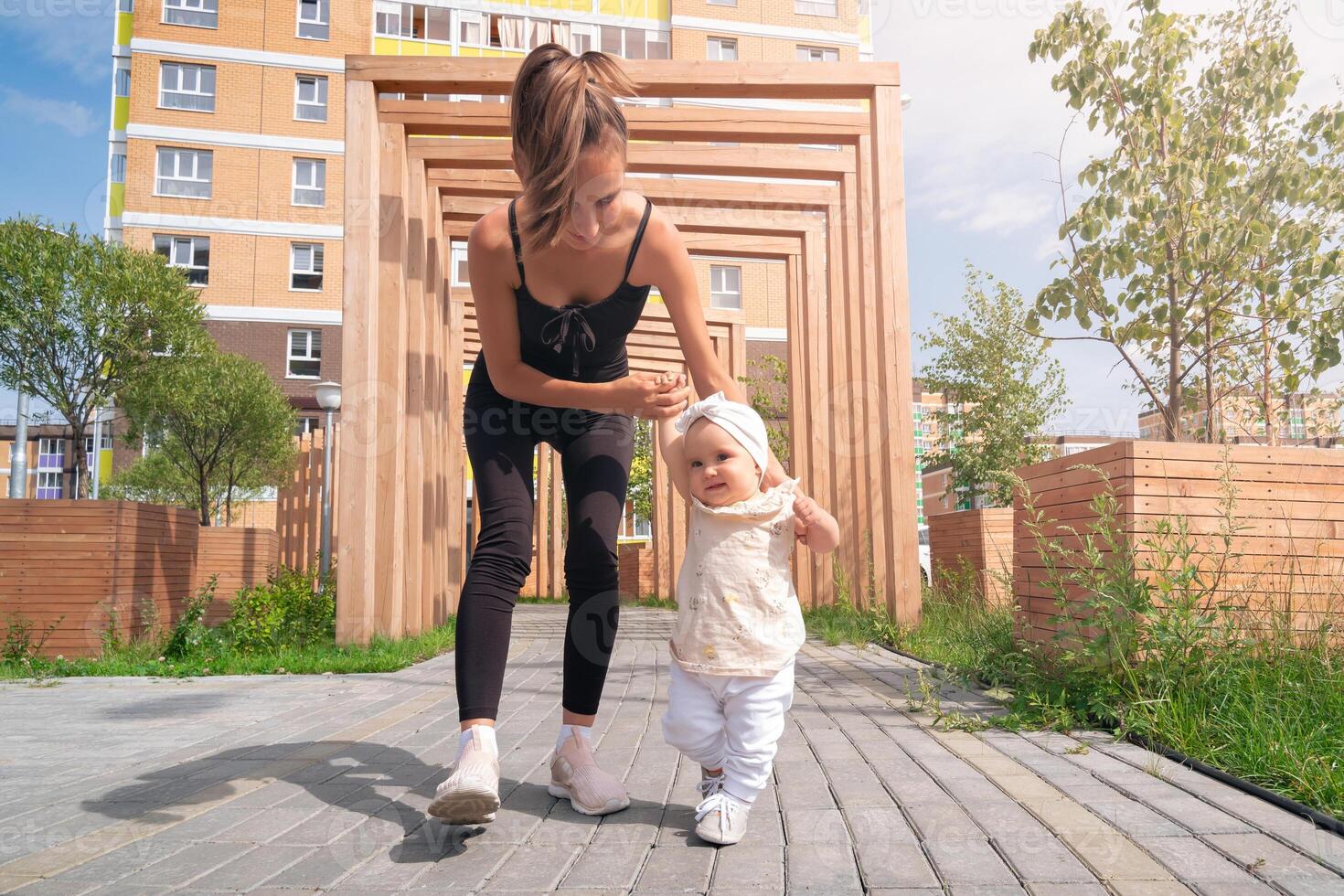 mom and toddler daughter walk in the city courtyard, child learns to walk photo