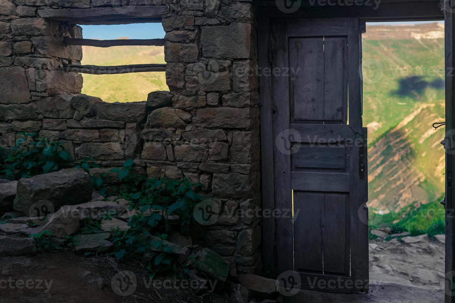 wooden door in the ruins of an abandoned house through which mountains are visible, in the ruins of the ghost village of Gamsutl in Dagestan photo