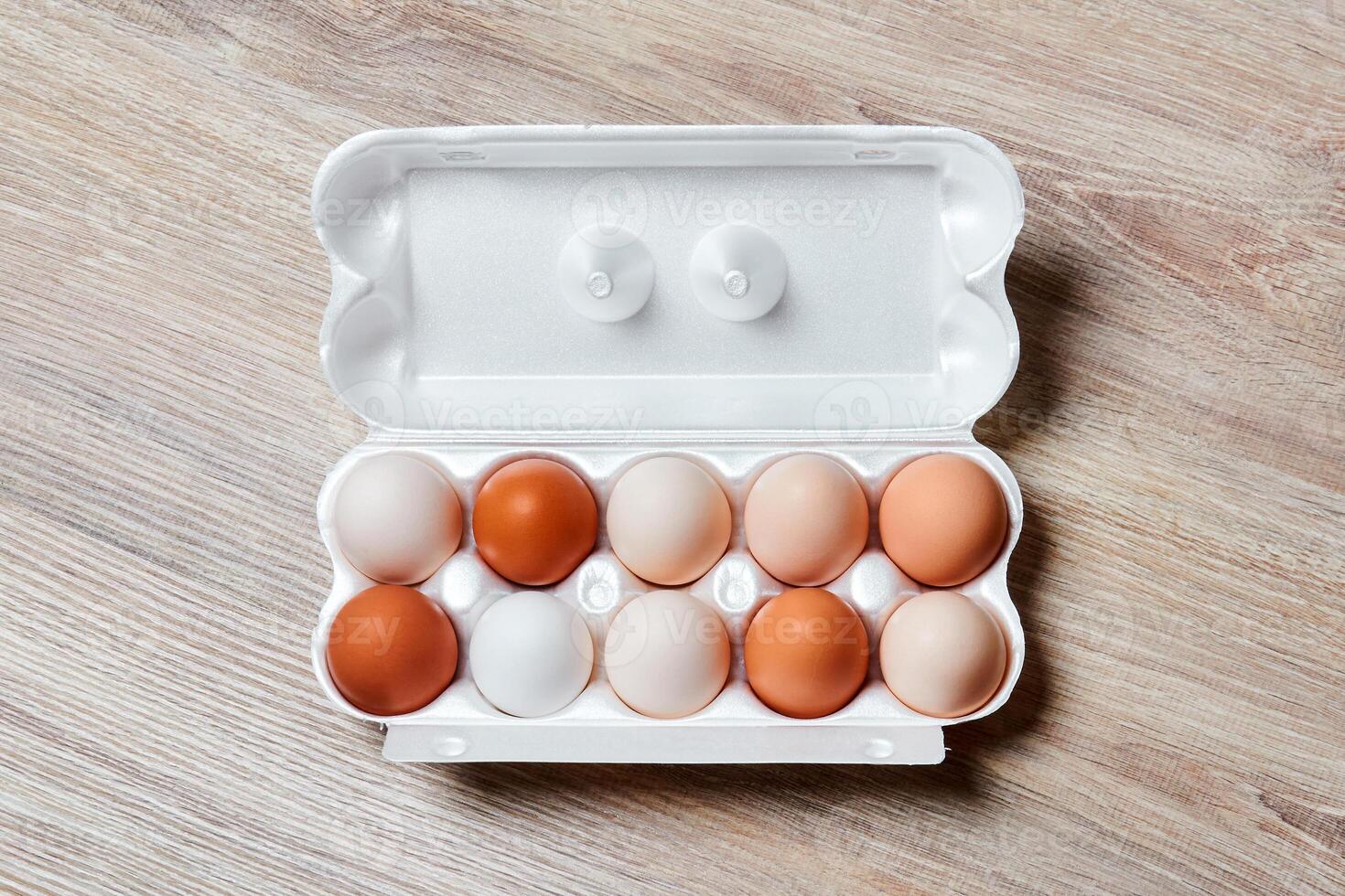 eggs of different colors from white to brown together in a crate on a wooden table surface photo
