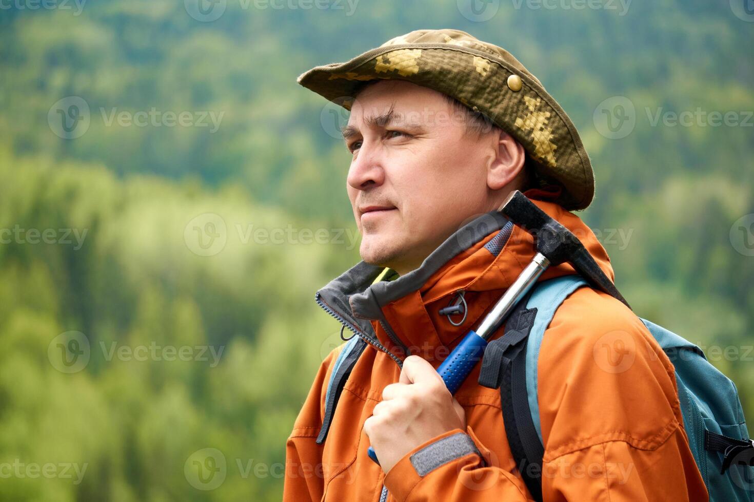 portrait of a man geologist with a backpack and a geological hammer against the wooded mountain landscape photo