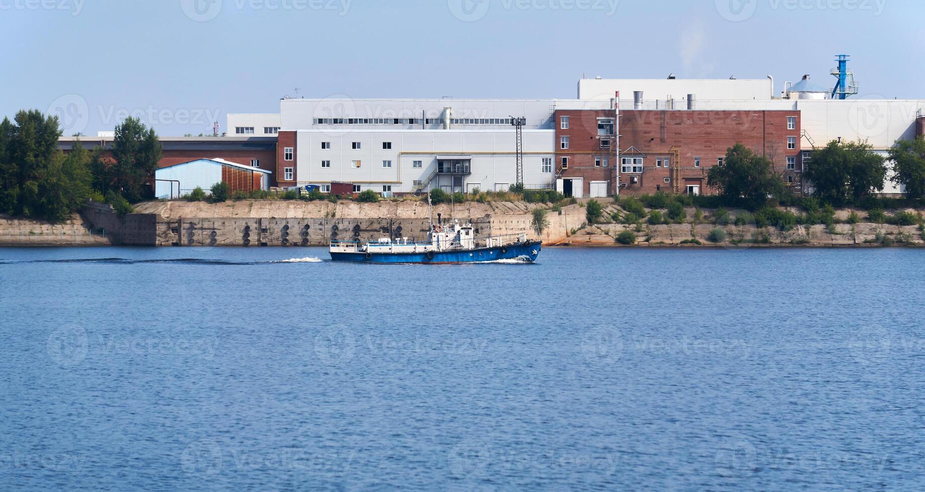 industrial landscape with a factory on the banks of the river, along which a motorship floats photo