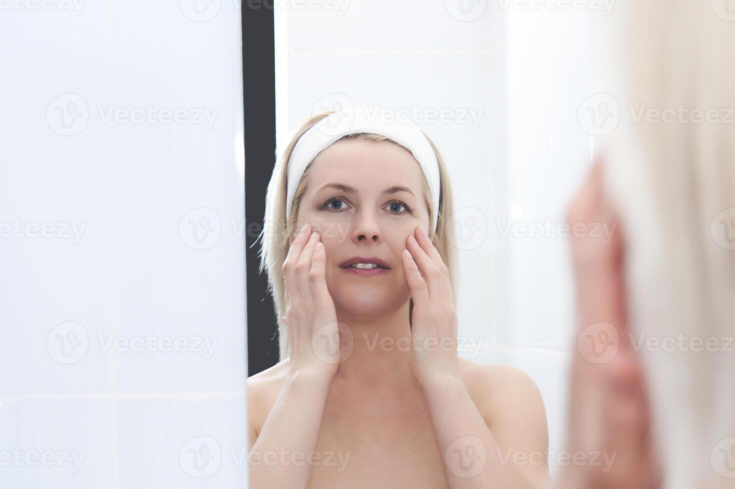 middle-aged woman makes self-massage of the face around the eyes in front of a mirror photo