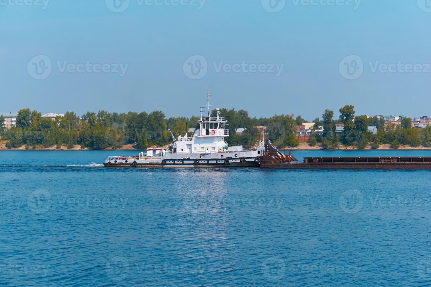 towboat pushes dry bulk cargo barge on the river past the city coast photo