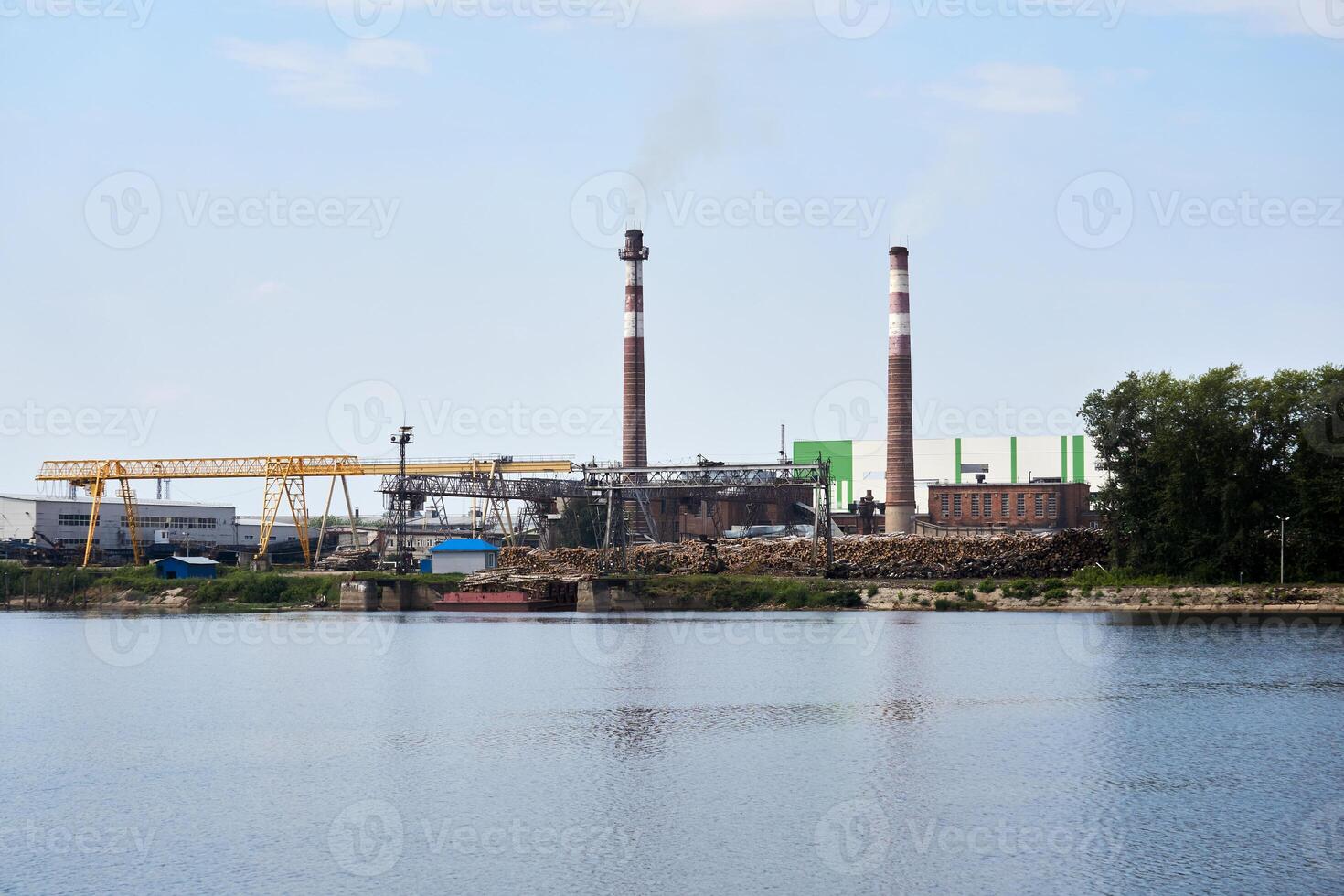 industrial paisaje, pulpa y papel molino con pilas de registros en el río banco foto