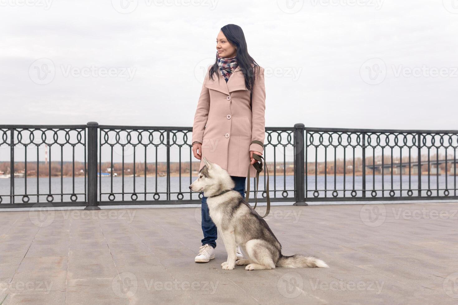 young woman with a husky dog walking on the city embankment in an autumn day photo
