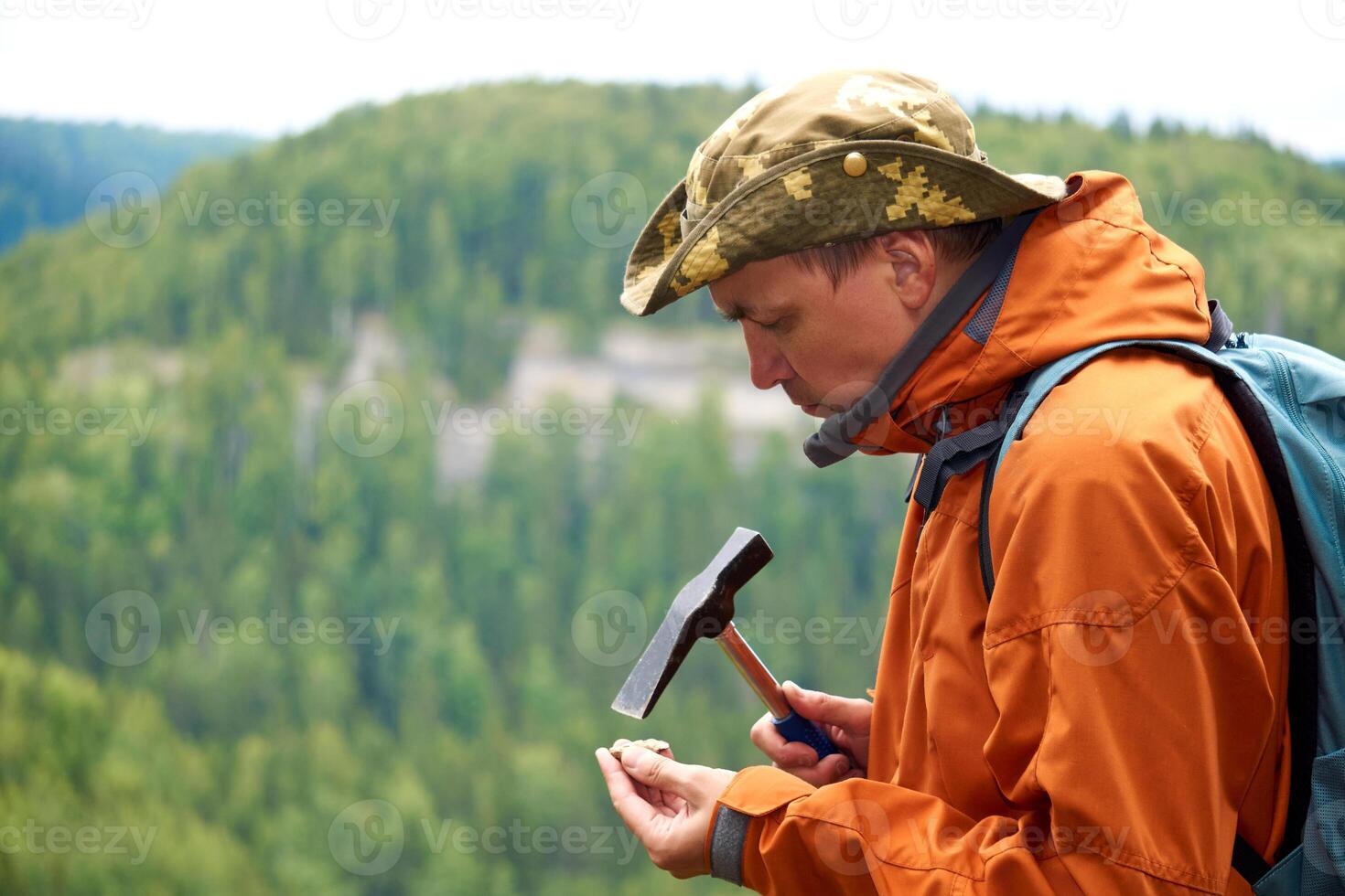 man geologist on an expedition examines a stone for hardness with a hammer photo