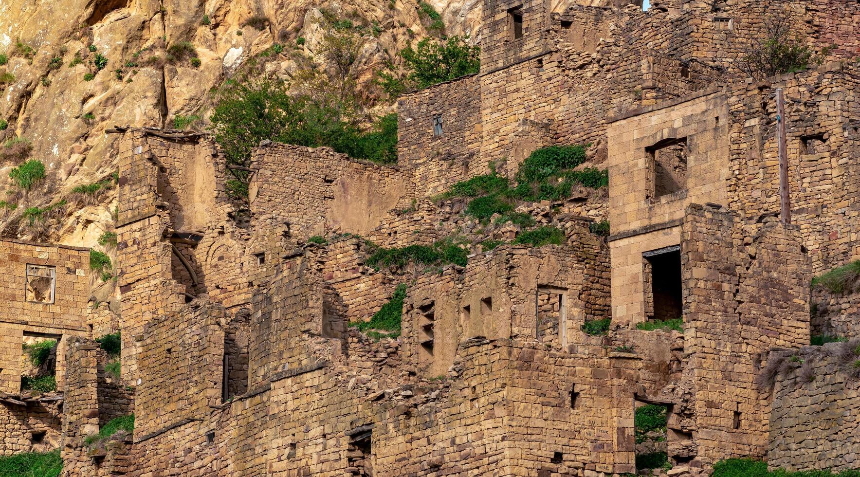 ruins of stone houses attached to the rock in the depopulated village of Gamsutl in the sunset rays photo
