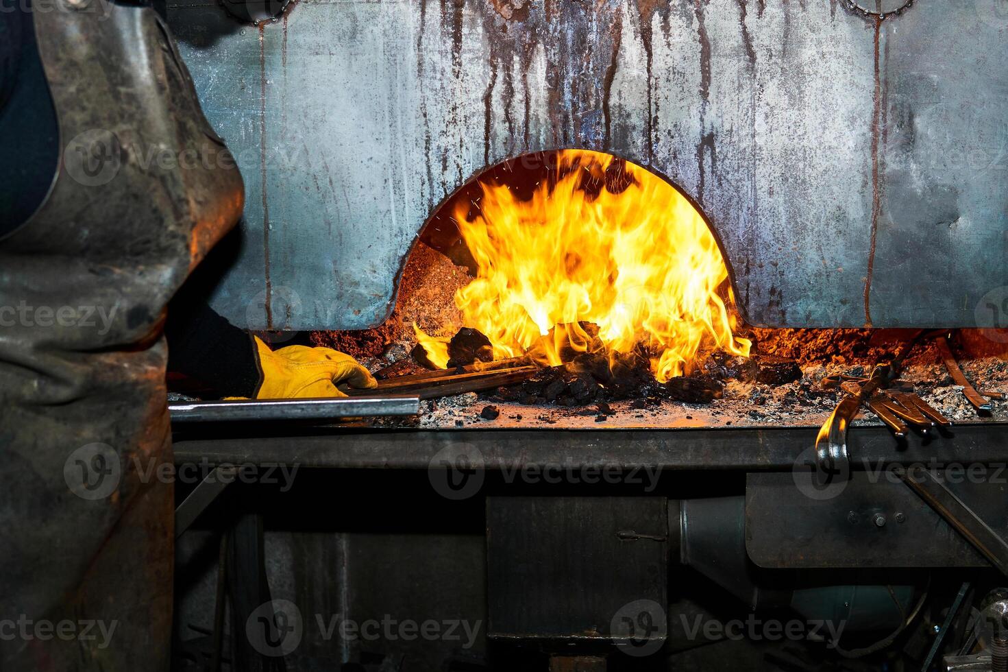 female metal artist pulls a workpiece from a blacksmith's furnace photo