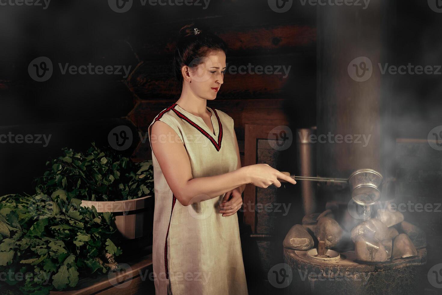 woman in a bath pours water on hot stones on the stove photo
