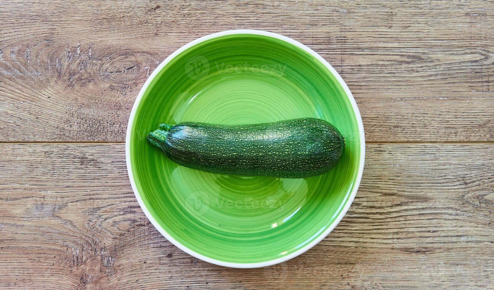 green zucchini squash with patterned skin on a green plate on a wooden tabletop photo