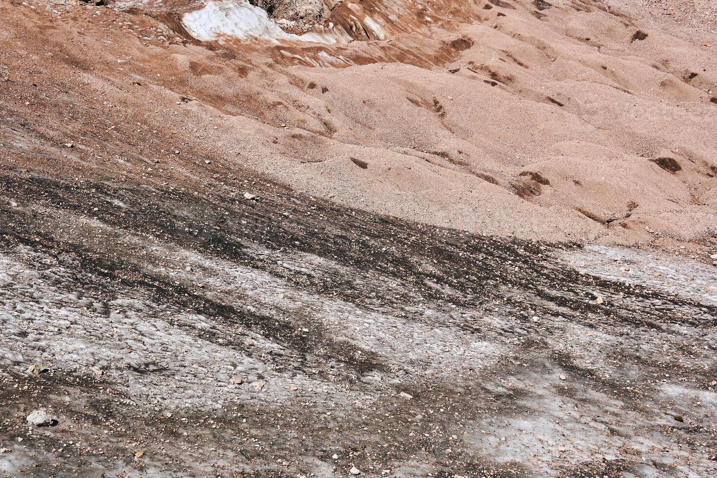 almost melted glacier at the foot of a cliff in the highlands and sand in a place where ice is gone photo