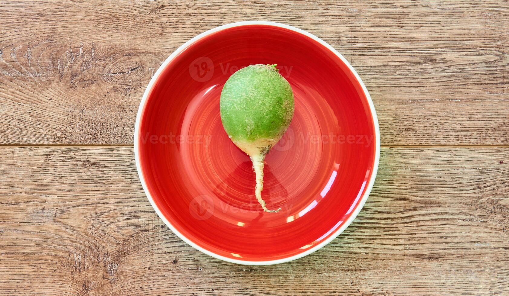 big green radish on a red plate on a wooden tabletop photo