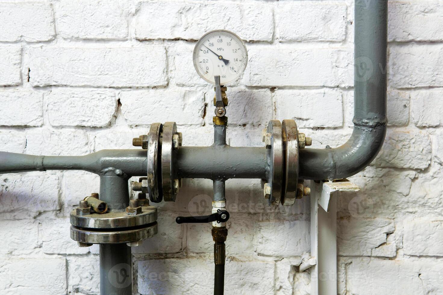 heating pipe with pressure gauge, valve and fittings, against a brick wall photo