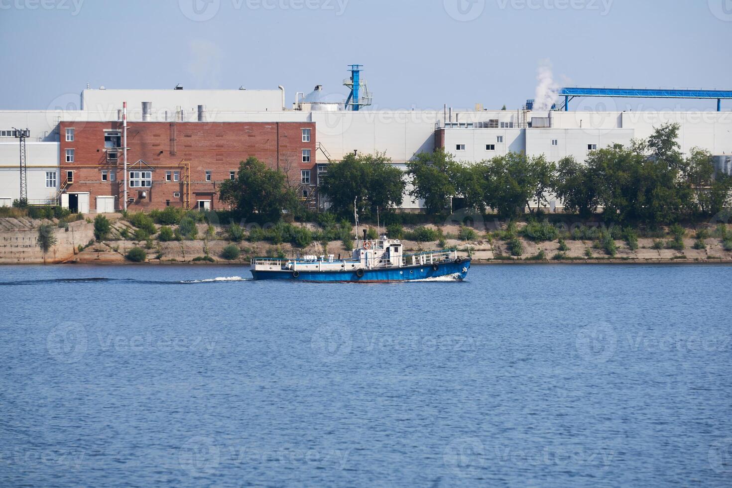 industrial landscape with a factory on the banks of the river, along which a motorship floats photo