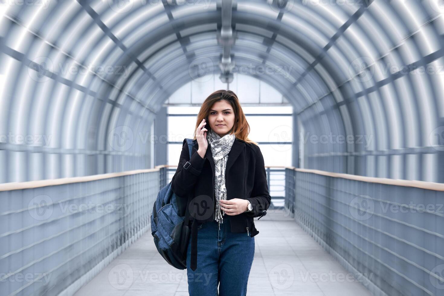 young woman is walking rapidly along the covered pedestrian overpass, talking on the phone photo