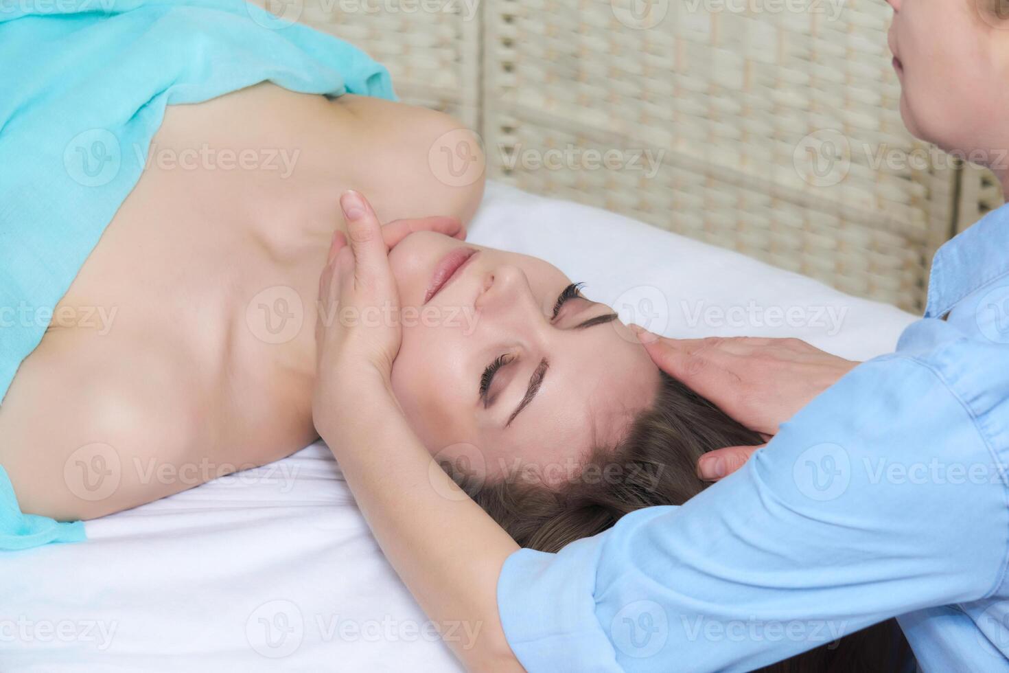 professional female beautician doing facial massage to woman in spa salon photo