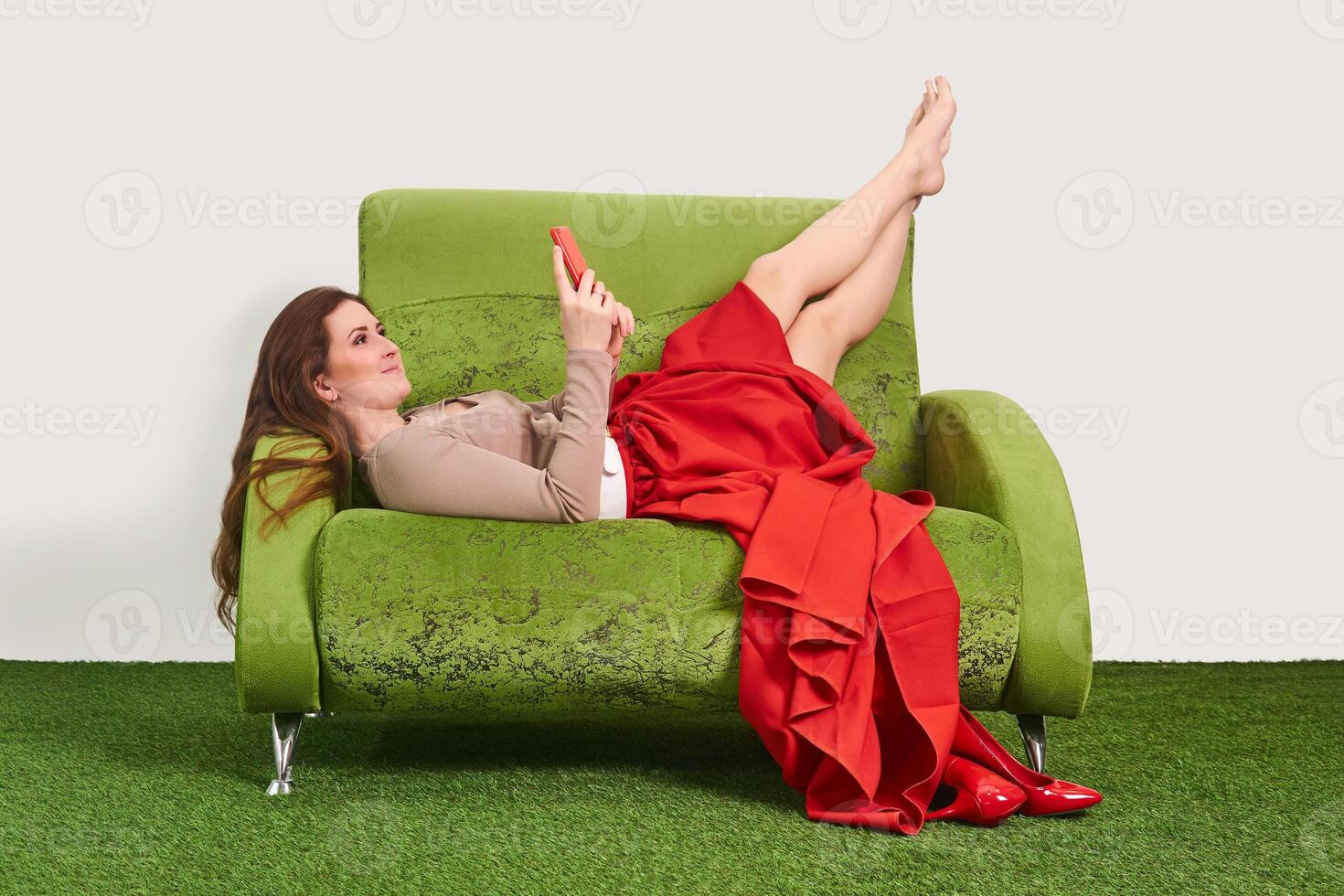 woman model looking into a smartphone while relaxing on the couch with legs raised upside down in between shoots photo