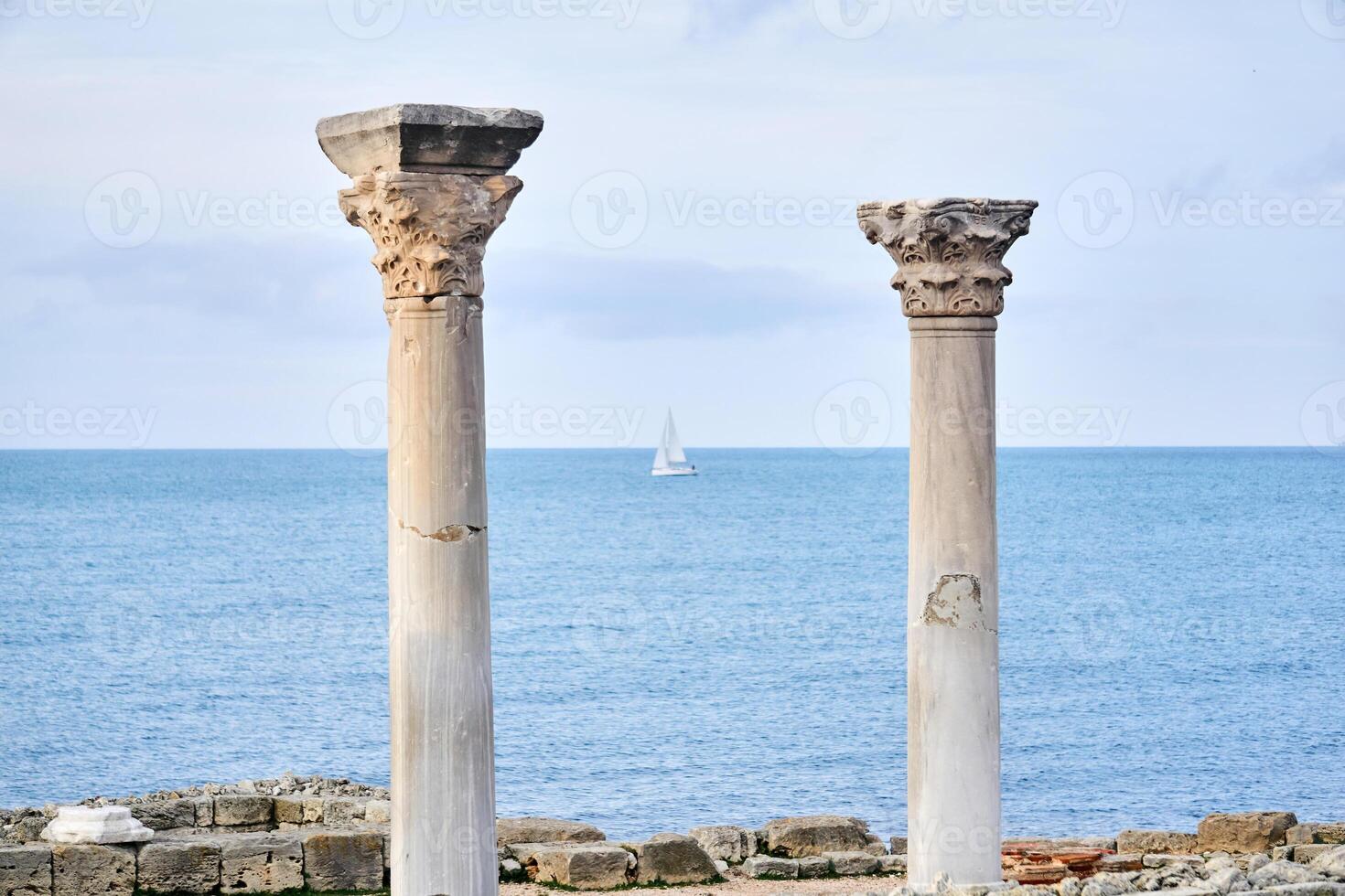 two dilapidated antique columns against the background of the sea, where you can see a blurred sailing ship photo