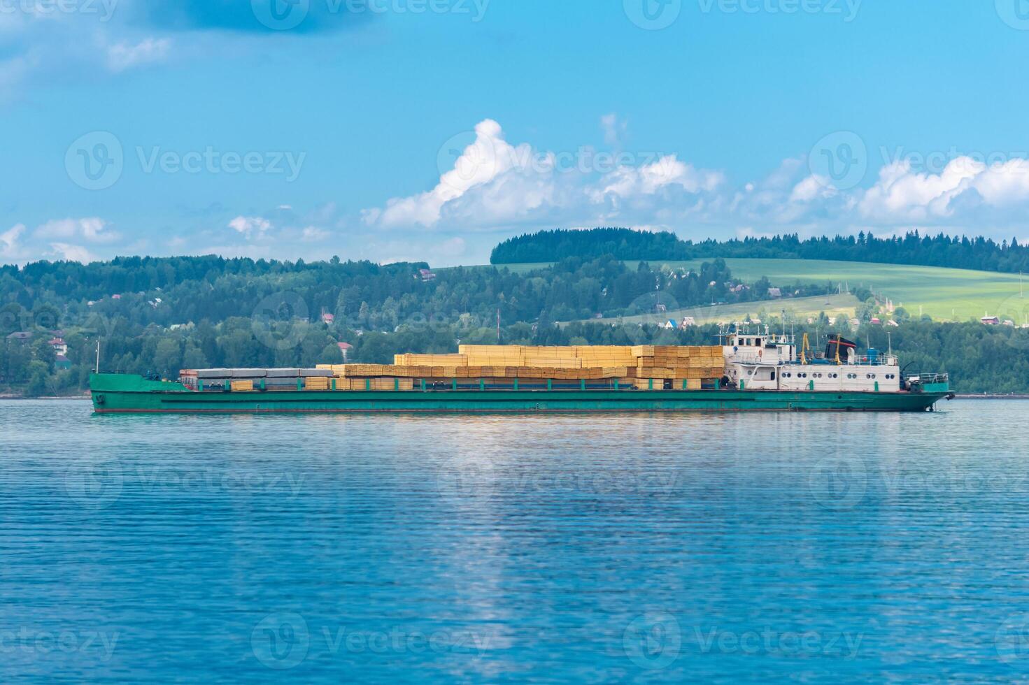 cargo ship loaded with lumber follows a wide river on a sunny day photo