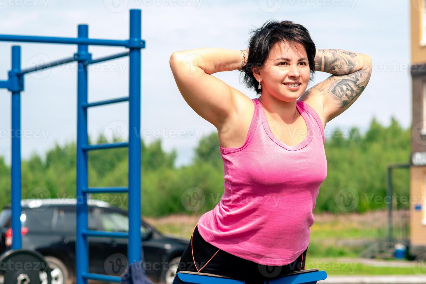 young woman shakes her back muscles using an outdoor exercise machine hyper extension bench photo
