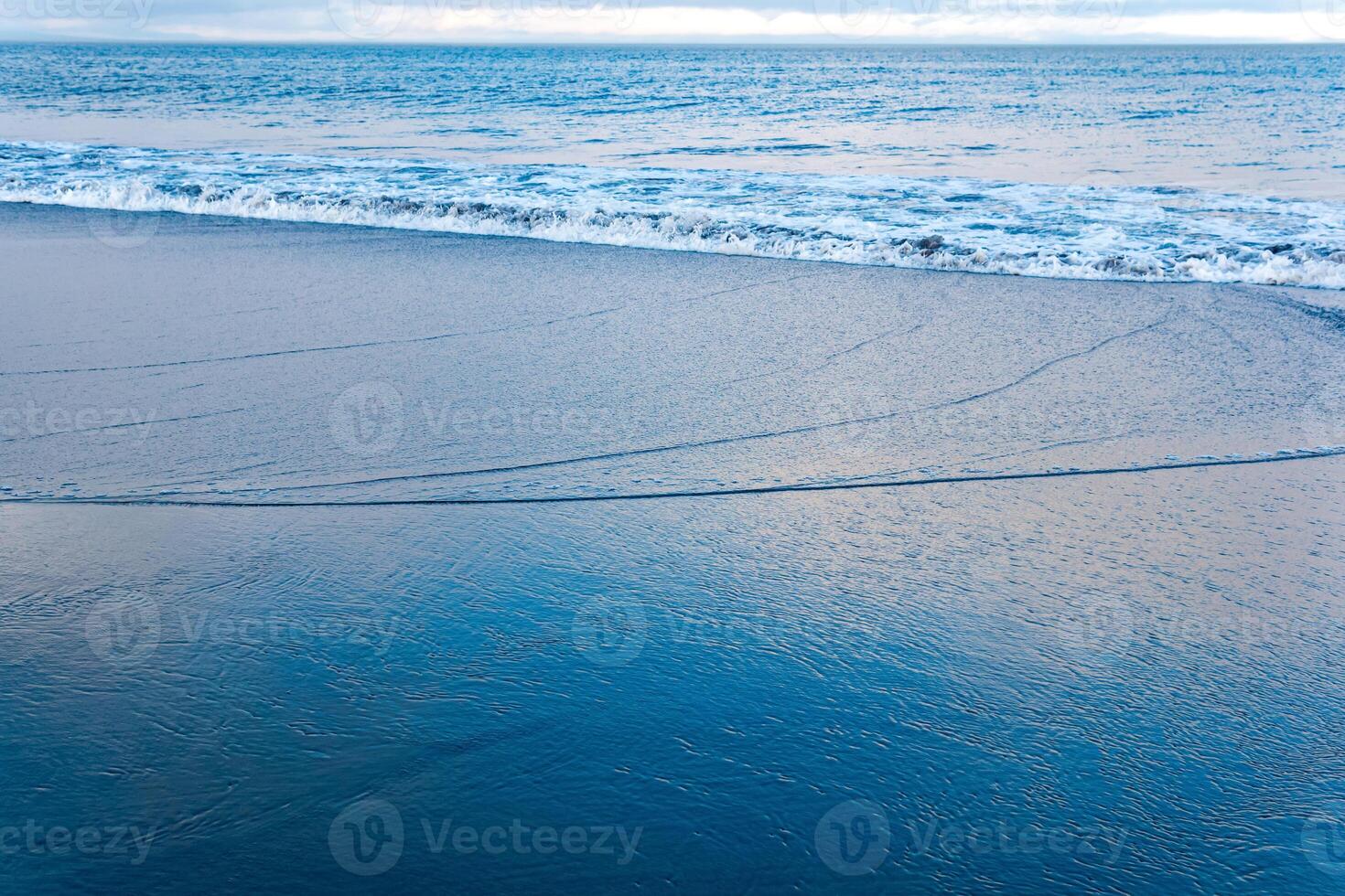 ocean beach with a wave coming back, in which the sky is reflected photo