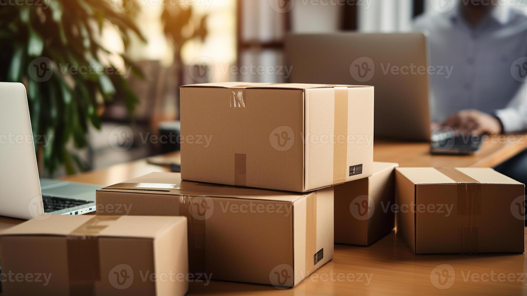 cardboard boxes on the table with laptop and man working in the background photo