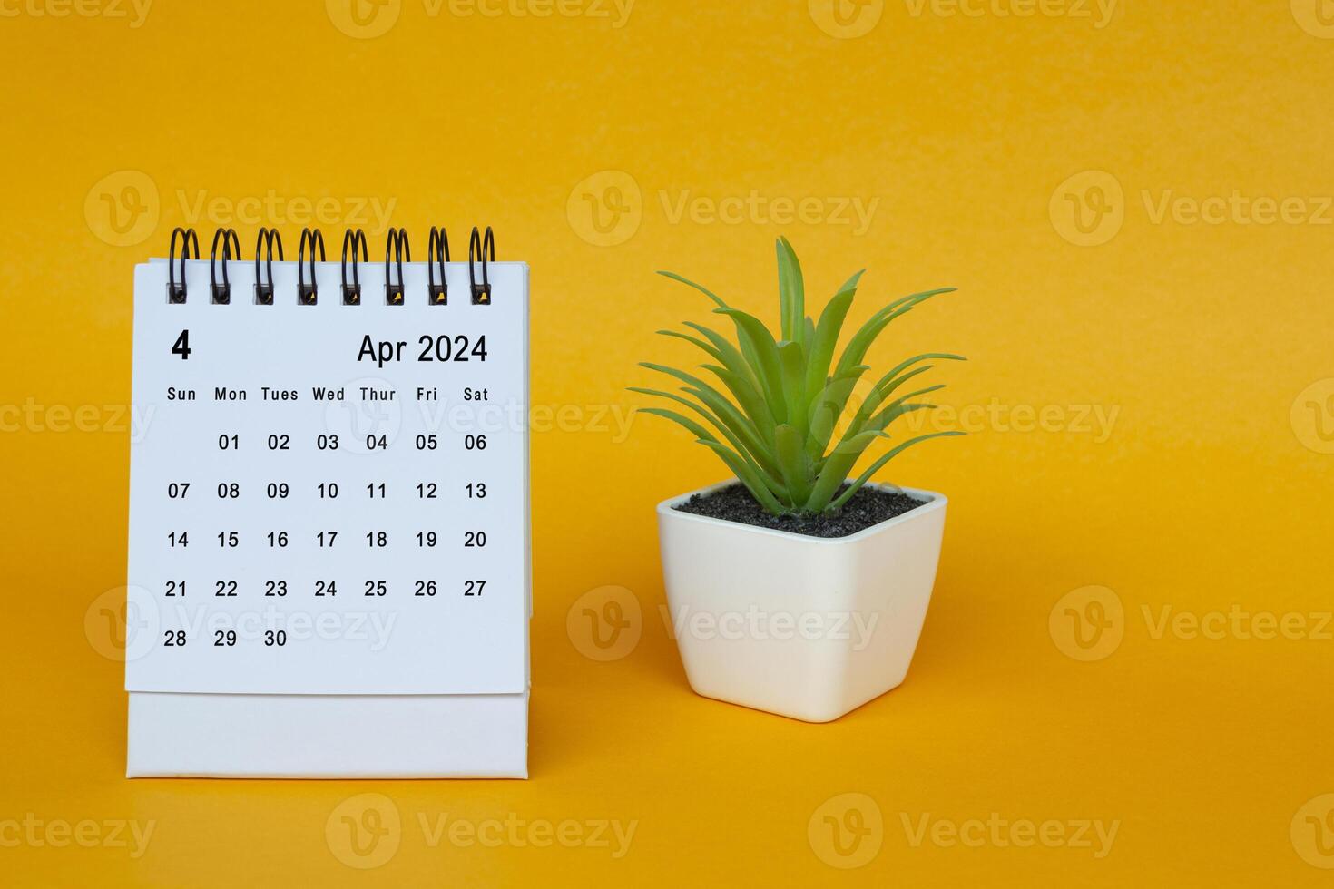 April 2024 desk calendar with potted plant on yellow background. photo