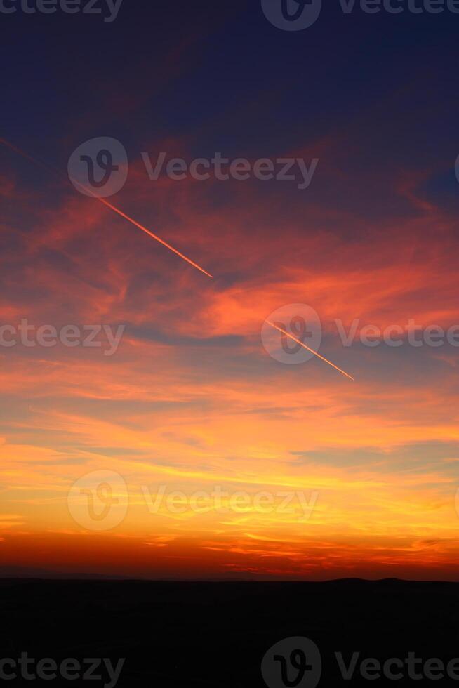 airplane and its trail in the sky. clouds and different color tones in the sky at sunset. Amazing and incredible sunset. photo