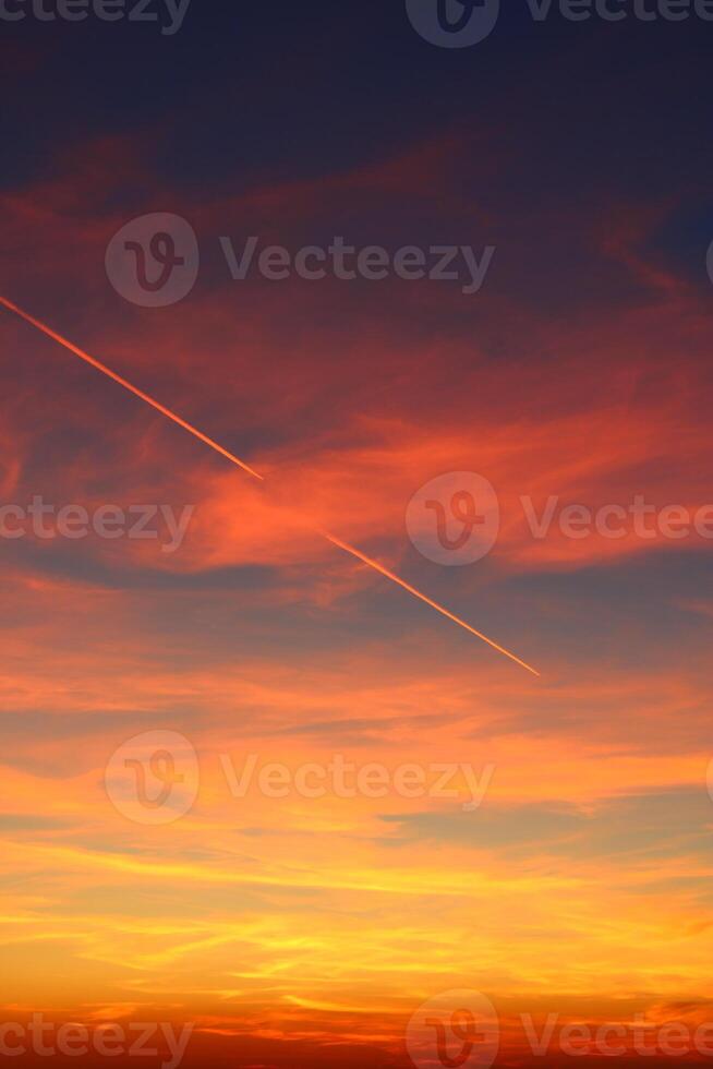airplane and its trail in the sky. clouds and different color tones in the sky at sunset. Amazing and incredible sunset. photo
