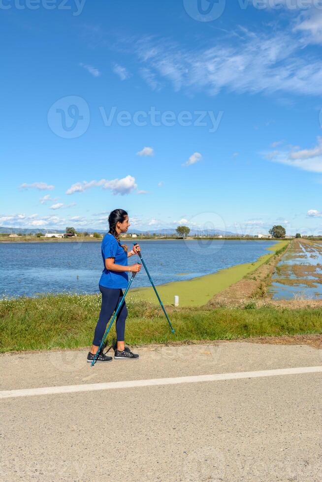 Hispanic latin woman walking with trekking poles in the Ebro Delta natural park,Tarragona, Catalonia, Spain, photo