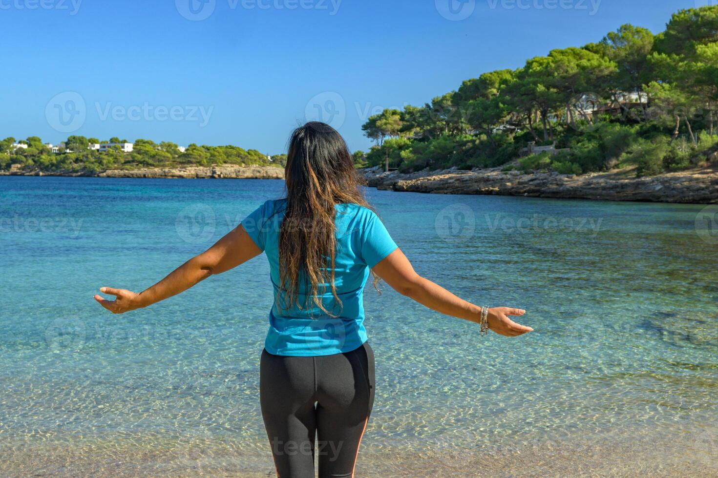 Latina woman, seen from behind, in sportswear, looking at the sea, breathing deeply. photo