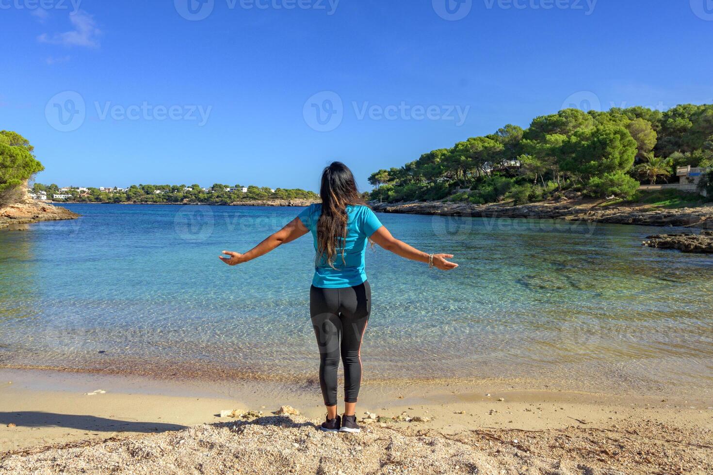 latina mujer, en ropa de deporte en su atrás, en el apuntalar de el playa mirando a el mar respiración profundamente. foto