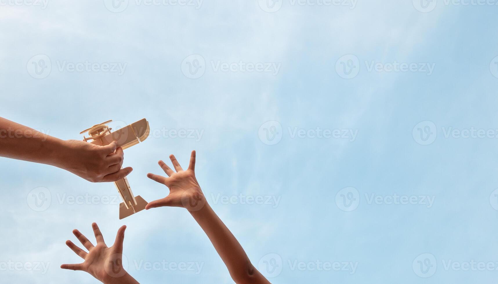 Child Holding a Wooden Airplane Model High in the Sky photo
