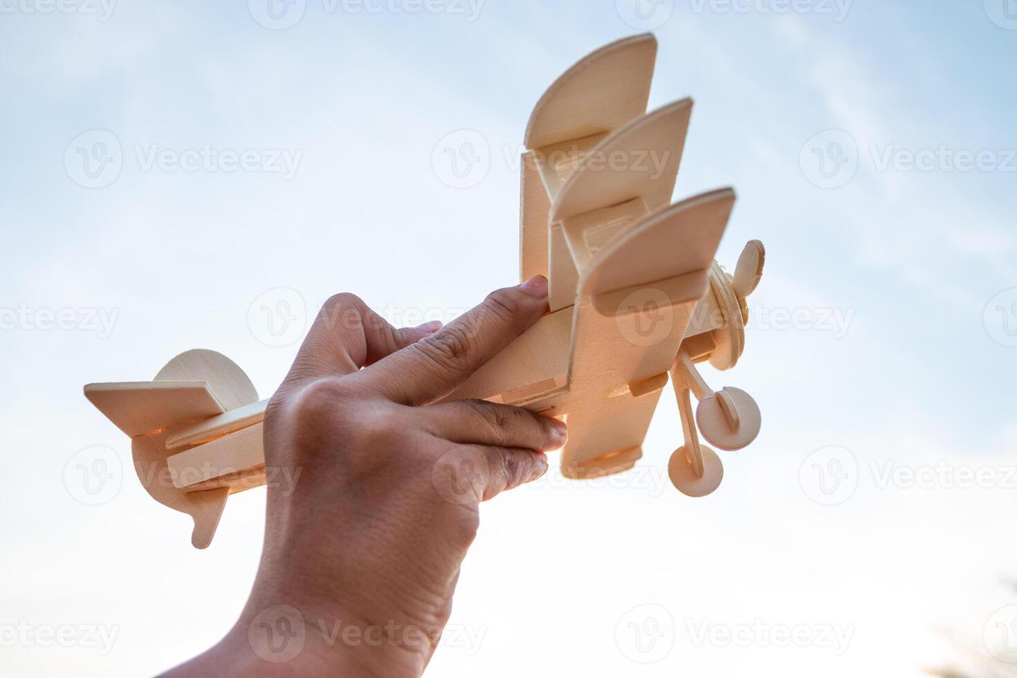 Child Holding a Wooden Airplane Model High in the Sky photo