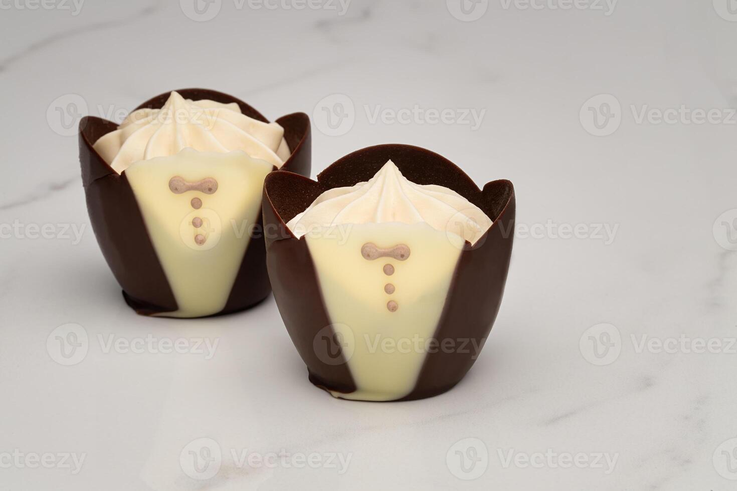 Dark chocolate tuxedo cups filled with vanilla mousse on a marble surface photo