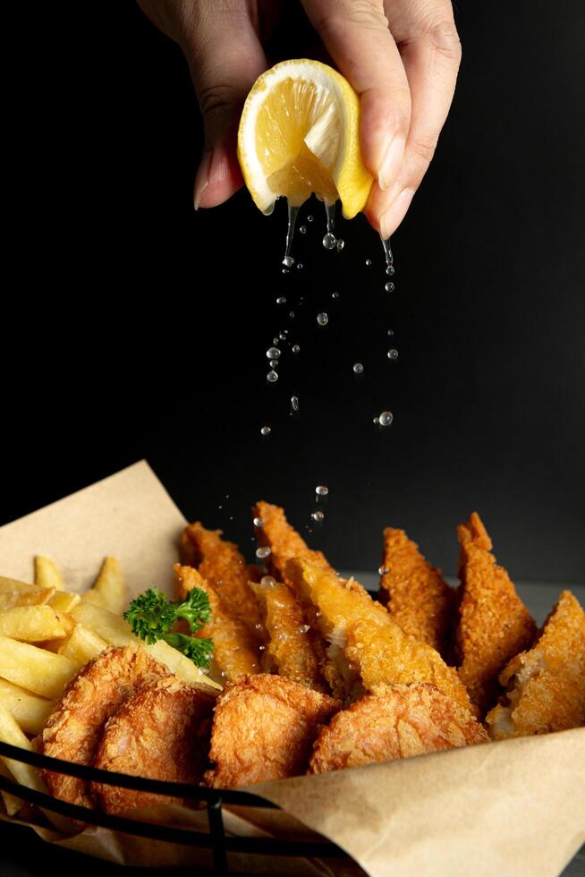 pescado y papas fritas en negro antecedentes con chapoteo limón en mano foto