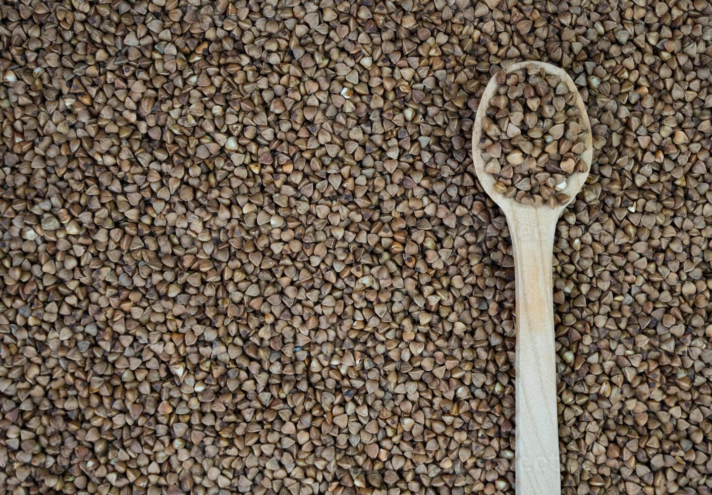 Buckwheat in a wooden spoon on scattered grains of buckwheat. Top view. Copy space. Banner. Close-up. Selective focus. photo