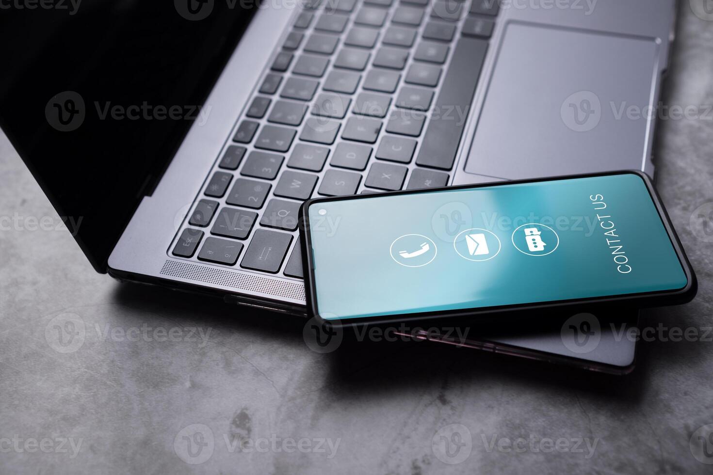Contact us or customer support hotline concept. Smartphone resting on laptop with contact icons on screen. Email, address, live chat, call. Helpdesk advice online support. photo