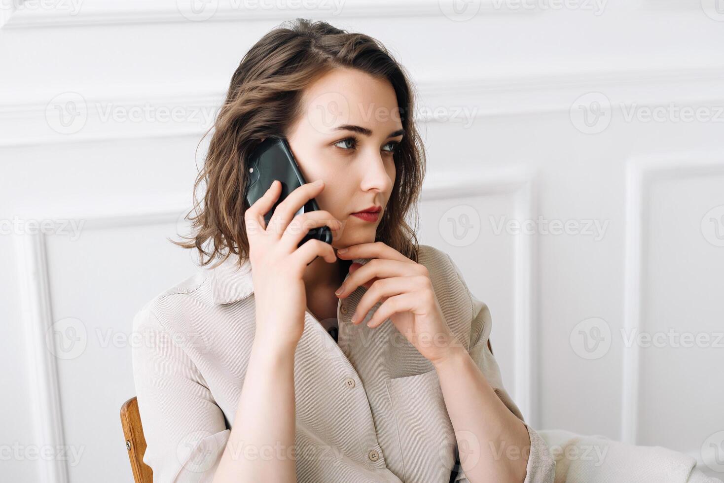 pensativo milenario mujer se involucra en un teléfono llamar, negociaciones atentamente, contemplativamente sentado en un silla, transporte un sentido de gravedad y reflexivo conversacion foto