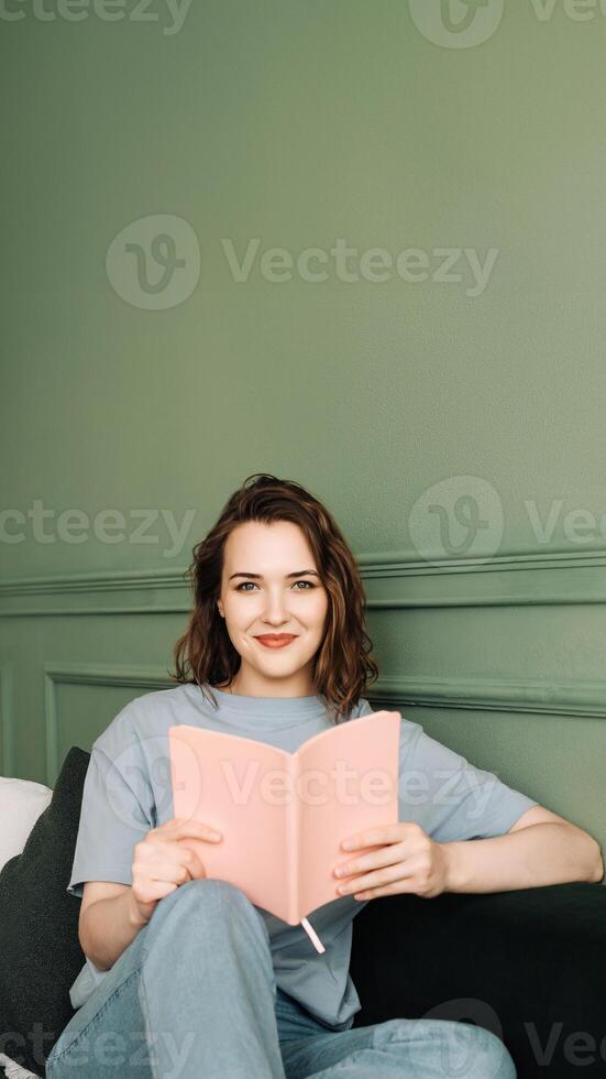 Happy young woman reading a book sitting comfortably on the couch enjoying a relaxing evening. Relaxed young woman enjoying a relaxing evening reading sitting on the couch. Rest and relaxation photo
