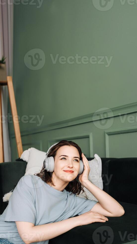 frío tiempo. alegre mujer escuchando a música en sofá con inalámbrico auriculares. ocio momentos contenido mujer en sofá escuchando a música vía inalámbrico auriculares foto