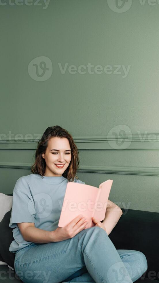 Joyful millennial young woman reading a book while relaxing on a couch in a cozy living room photo