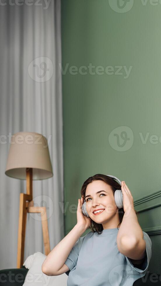 Happy young woman wearing wireless headphones listening to music while enjoying some free time on the couch. Joyful Moments. Woman Relaxing and Listening to Music on the Sofa photo