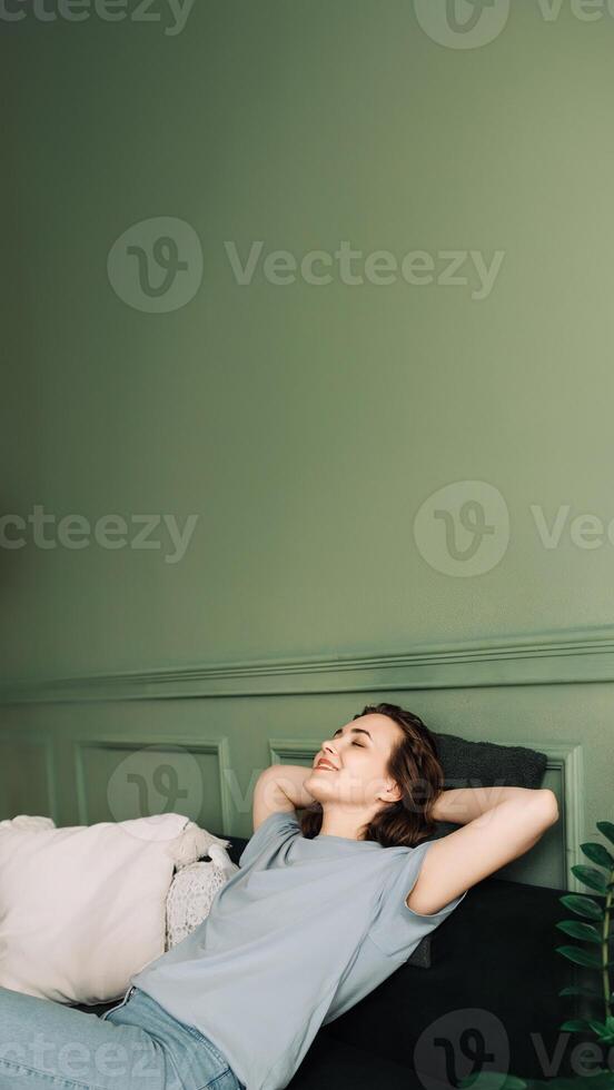 un alegre joven de edad mediana mujer con su ojos cerrado disfrutando dormir en el vivo habitación sofá. feliz sueño. alegre de edad mediana mujer relaja en vivo habitación sofá foto